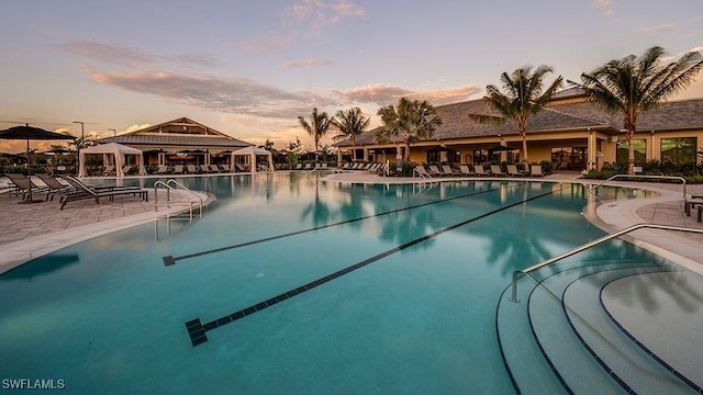 pool at dusk with a gazebo, a community pool, and a patio area