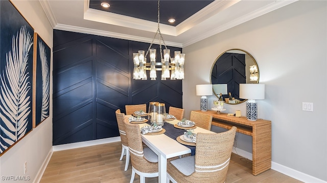 dining space featuring light wood-type flooring, a tray ceiling, an inviting chandelier, and ornamental molding