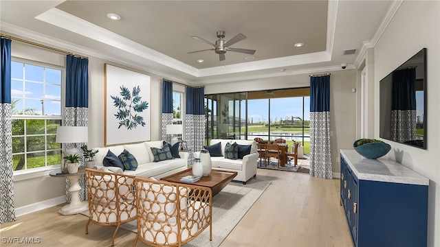 living area with a tray ceiling, baseboards, light wood-style flooring, and ornamental molding