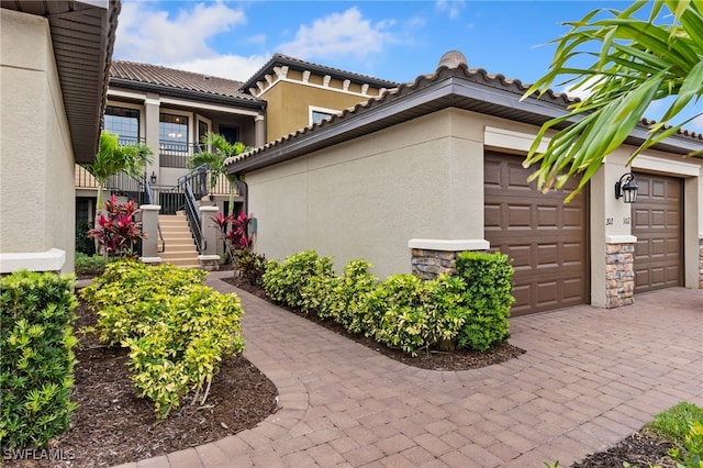 view of side of property with stucco siding, stone siding, an attached garage, and stairway