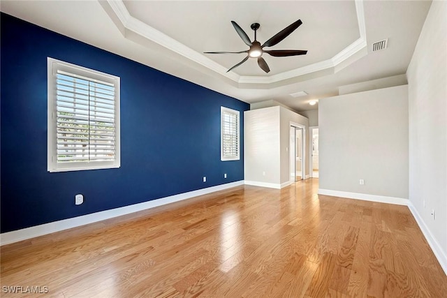 spare room with a raised ceiling, wood finished floors, visible vents, and baseboards