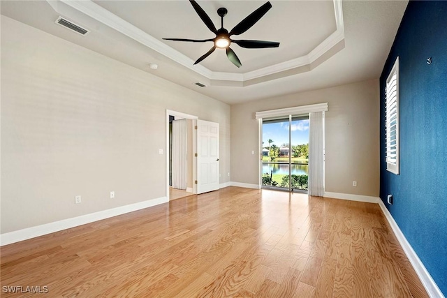 empty room featuring visible vents, baseboards, light wood-style floors, and a tray ceiling