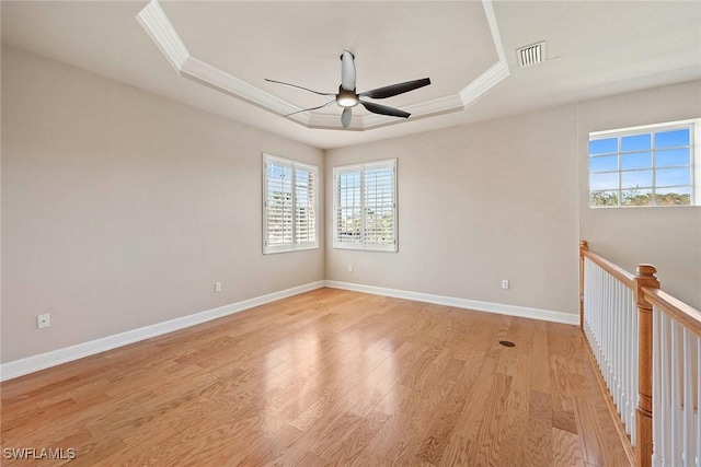 spare room featuring visible vents, a raised ceiling, light wood-style floors, and crown molding