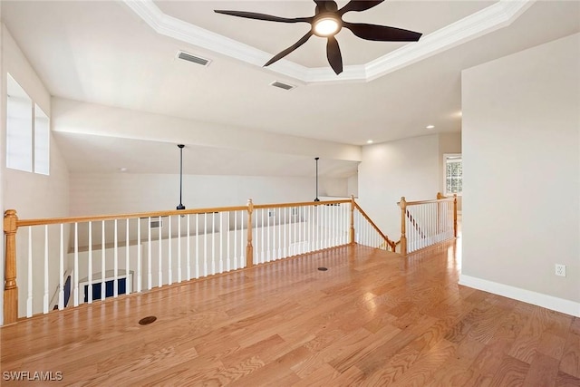 empty room featuring a tray ceiling, visible vents, wood finished floors, and crown molding