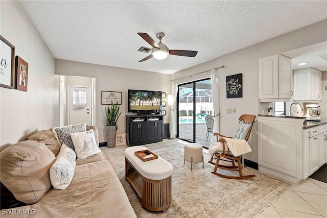 living area featuring light tile patterned flooring, a ceiling fan, visible vents, and a textured ceiling