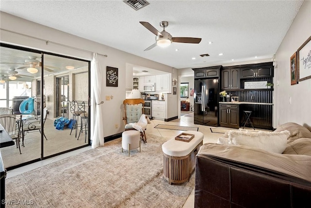 living area featuring light tile patterned floors, baseboards, visible vents, ceiling fan, and a textured ceiling