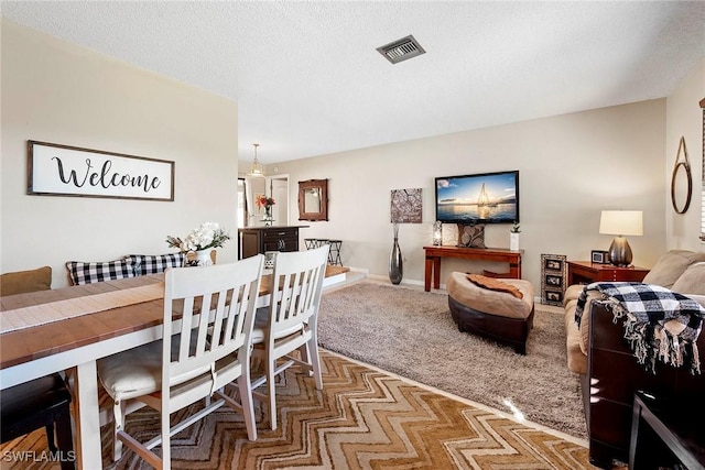 carpeted dining space with visible vents, baseboards, and a textured ceiling