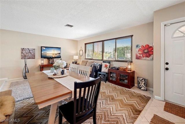 dining area with light tile patterned flooring, visible vents, a textured ceiling, and baseboards