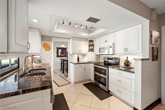 kitchen with double oven range, white microwave, visible vents, a tray ceiling, and a sink