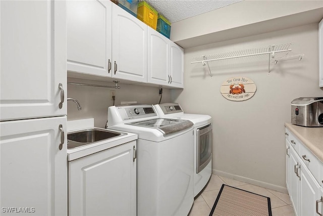 clothes washing area featuring light tile patterned flooring, cabinet space, a sink, a textured ceiling, and washing machine and dryer