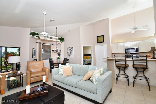 living room with light tile patterned floors, ceiling fan with notable chandelier, visible vents, and high vaulted ceiling