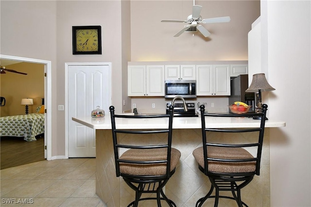 kitchen with a kitchen bar, white cabinetry, appliances with stainless steel finishes, light tile patterned floors, and a towering ceiling