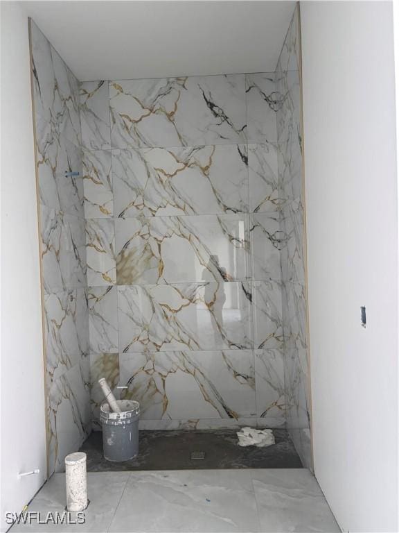 bathroom featuring a marble finish shower and stone wall