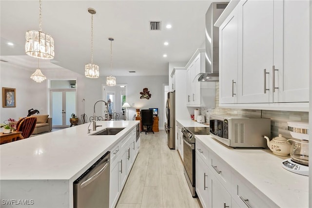 kitchen featuring visible vents, a sink, stainless steel appliances, wall chimney exhaust hood, and light countertops