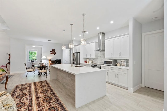 kitchen with a center island with sink, a sink, stainless steel appliances, wall chimney range hood, and tasteful backsplash