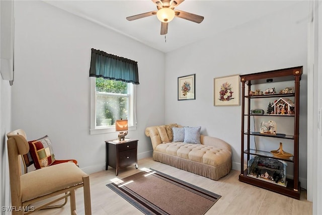 living area with baseboards, light wood-type flooring, and ceiling fan