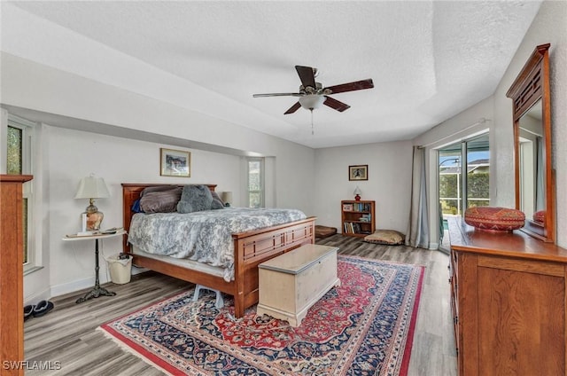 bedroom featuring access to exterior, wood finished floors, baseboards, and a textured ceiling