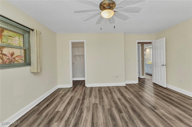 unfurnished bedroom featuring a textured ceiling, wood finished floors, a closet, baseboards, and a spacious closet