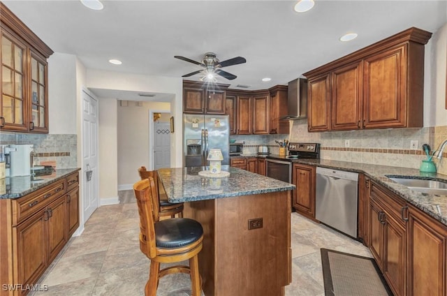 kitchen featuring a sink, a kitchen breakfast bar, stainless steel appliances, dark stone counters, and wall chimney range hood