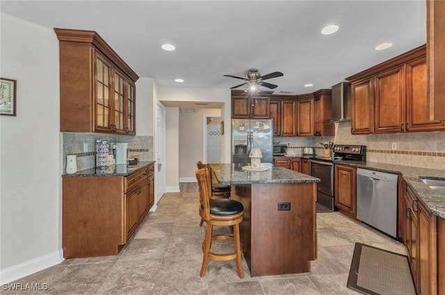 kitchen with dark stone countertops, a kitchen island, stainless steel appliances, glass insert cabinets, and wall chimney exhaust hood