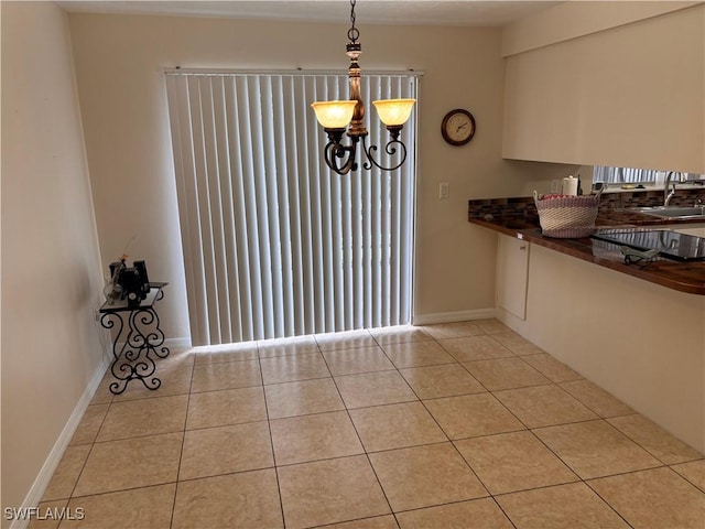 unfurnished dining area with a sink, light tile patterned floors, baseboards, and a chandelier