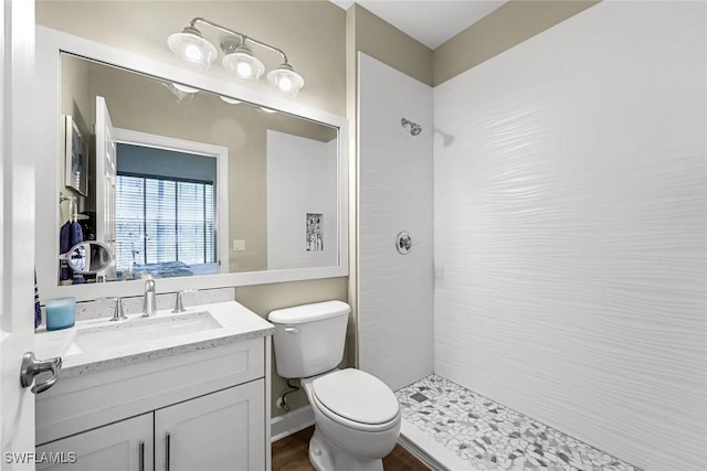 bathroom featuring baseboards, toilet, vanity, and a tile shower