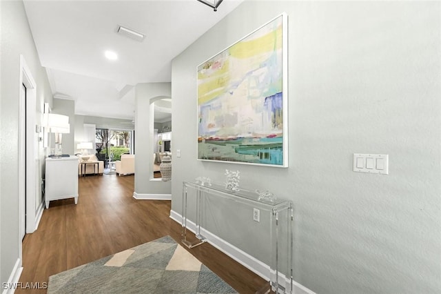 corridor featuring wood finished floors, arched walkways, visible vents, and baseboards