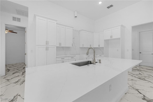 kitchen with visible vents, light stone countertops, white cabinets, marble finish floor, and a sink