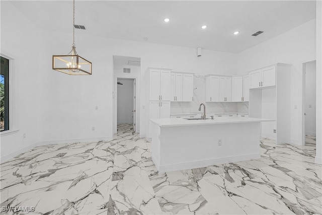 kitchen with visible vents, a center island with sink, light countertops, white cabinetry, and a sink