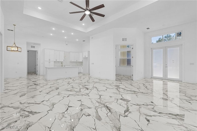 unfurnished living room with a towering ceiling, recessed lighting, french doors, a raised ceiling, and ceiling fan