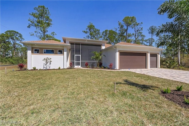 view of front of property with an attached garage, a sunroom, stucco siding, a front lawn, and decorative driveway