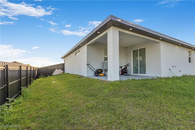 back of house featuring a lawn, a fenced backyard, and stucco siding