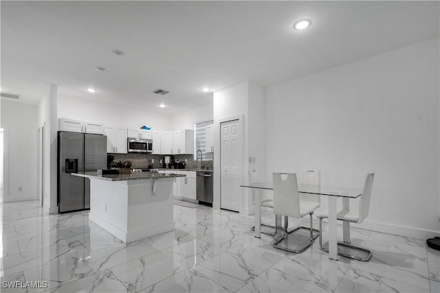 kitchen featuring a kitchen island, decorative backsplash, appliances with stainless steel finishes, white cabinets, and marble finish floor