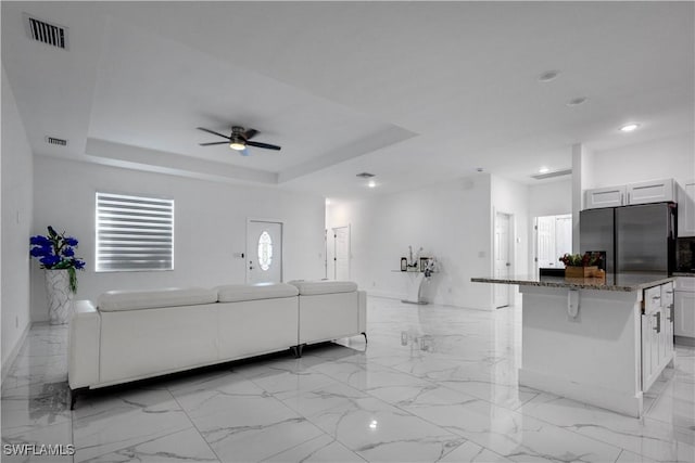 unfurnished living room with a tray ceiling, marble finish floor, and visible vents