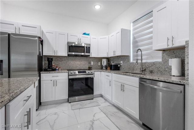 kitchen featuring marble finish floor, a sink, tasteful backsplash, stainless steel appliances, and light stone countertops