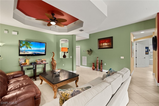 living area with ceiling fan, a tray ceiling, light tile patterned floors, and ornamental molding