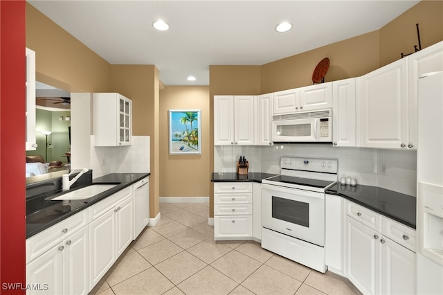 kitchen featuring tasteful backsplash, white appliances, dark countertops, and a sink