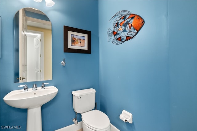 half bath with toilet, baseboards, and a sink