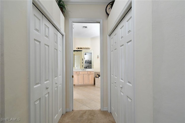 hallway featuring light tile patterned floors, light colored carpet, visible vents, and a sink