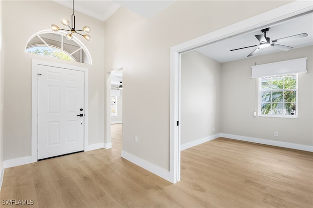 foyer entrance featuring baseboards, ornamental molding, ceiling fan with notable chandelier, and light wood-type flooring