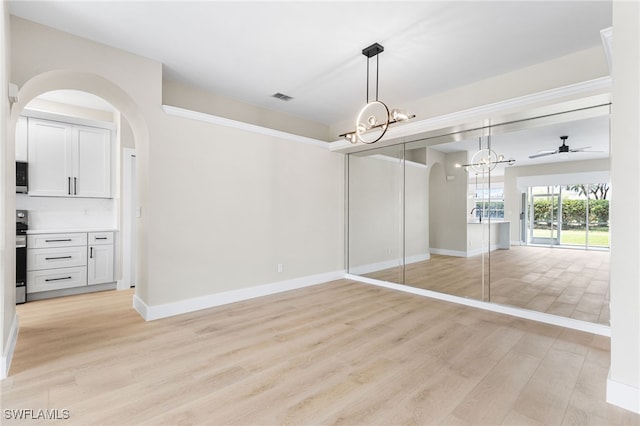 unfurnished dining area with visible vents, arched walkways, baseboards, ceiling fan with notable chandelier, and light wood finished floors