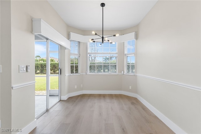 unfurnished dining area with light wood-style floors, baseboards, and a chandelier