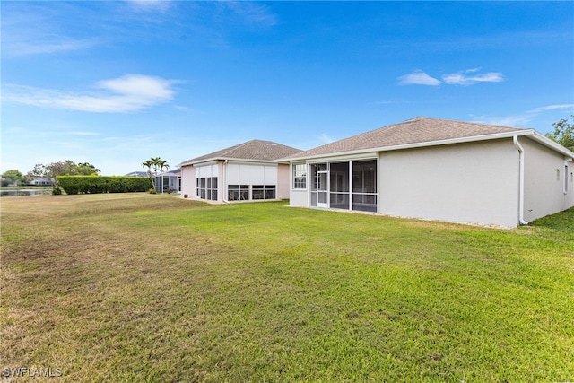rear view of property featuring a lawn, roof with shingles, a sunroom, and stucco siding