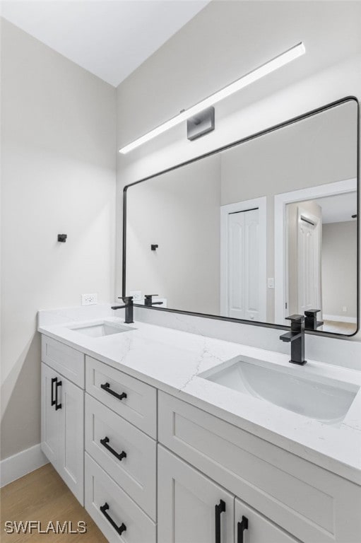 full bath with a sink, baseboards, double vanity, and wood finished floors