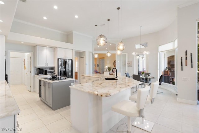 kitchen with stainless steel refrigerator with ice dispenser, a sink, crown molding, light tile patterned floors, and a large island with sink