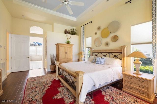 bedroom with multiple windows, a raised ceiling, baseboards, and wood-type flooring