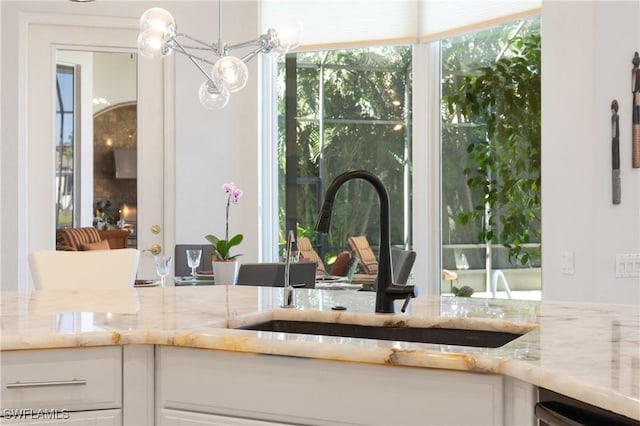 interior space featuring a notable chandelier, a sink, light stone counters, white cabinetry, and dishwasher