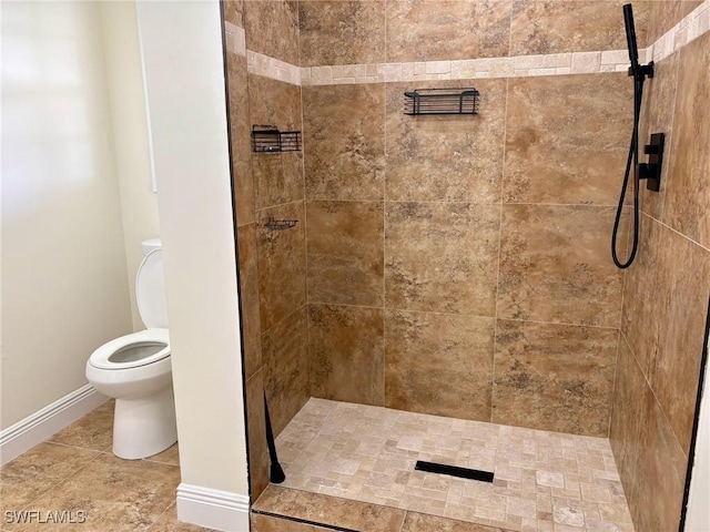 bathroom with toilet, baseboards, and tiled shower