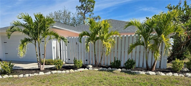 view of property hidden behind natural elements featuring a garage and fence