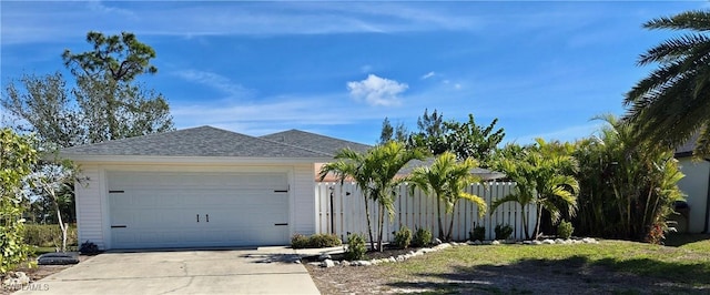 ranch-style house featuring roof with shingles, driveway, and fence